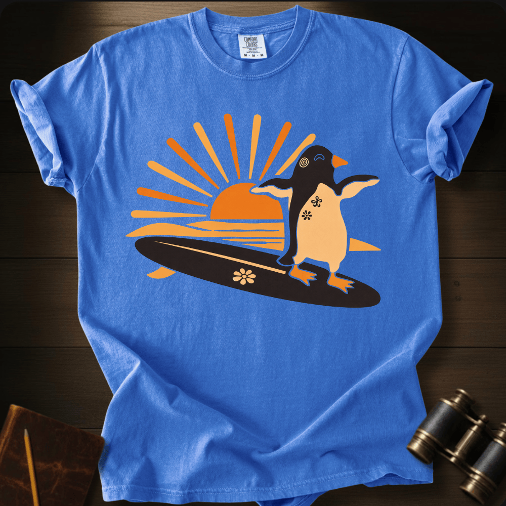 Full Sail Marine Sunset Surf penguin surfing graphic Comfort Colors t-shirt in flo blue – cute penguin on surfboard with sunset design – front view