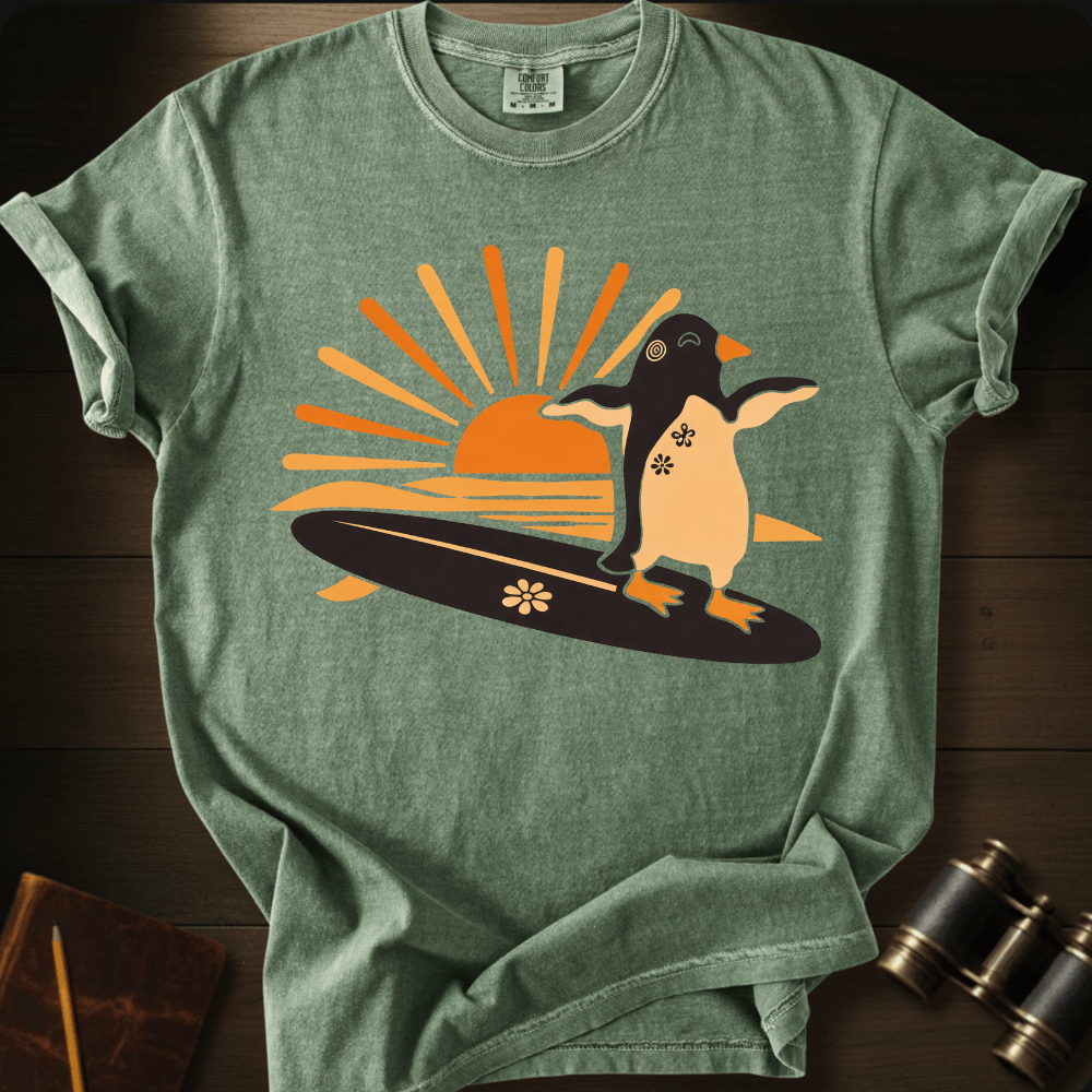 Full Sail Marine Sunset Surf penguin surfing graphic Comfort Colors t-shirt in hemp green – cute penguin on surfboard with sunset design – front view