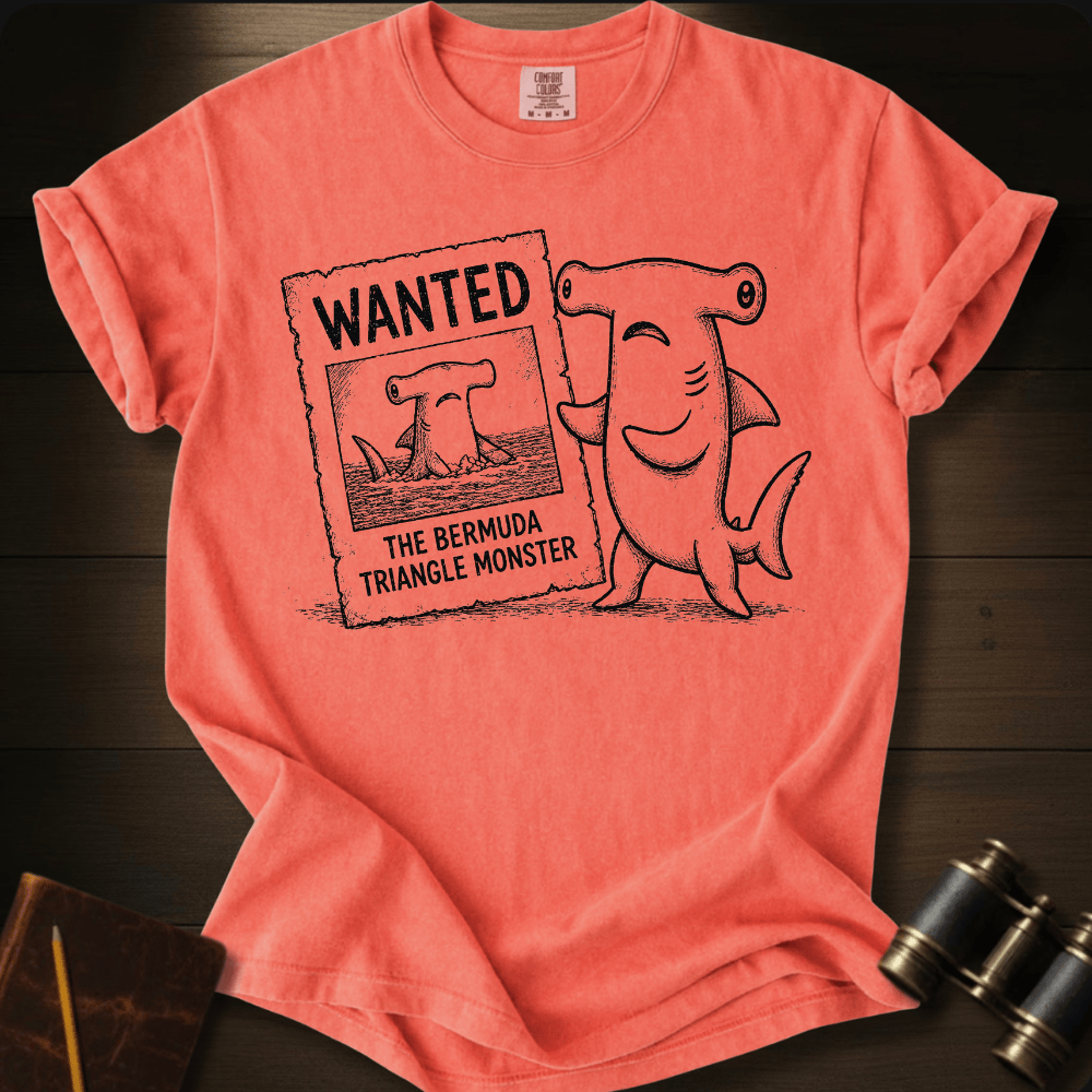 Coral Comfort Colors tee with a cartoon hammerhead shark holding a 'Wanted: The Bermuda Triangle Monster' poster.