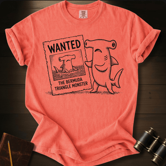 Coral Comfort Colors tee with a cartoon hammerhead shark holding a 'Wanted: The Bermuda Triangle Monster' poster.