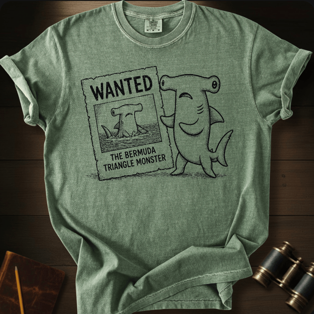 Moss Comfort Colors tee with a cartoon hammerhead shark holding a 'Wanted: The Bermuda Triangle Monster' poster.