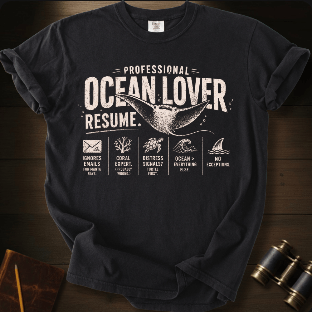 A black graphic t-shirt laid flat on a dark wood background. The shirt features a white distressed print that reads 'PROFESSIONAL OCEAN LOVER RESUME.