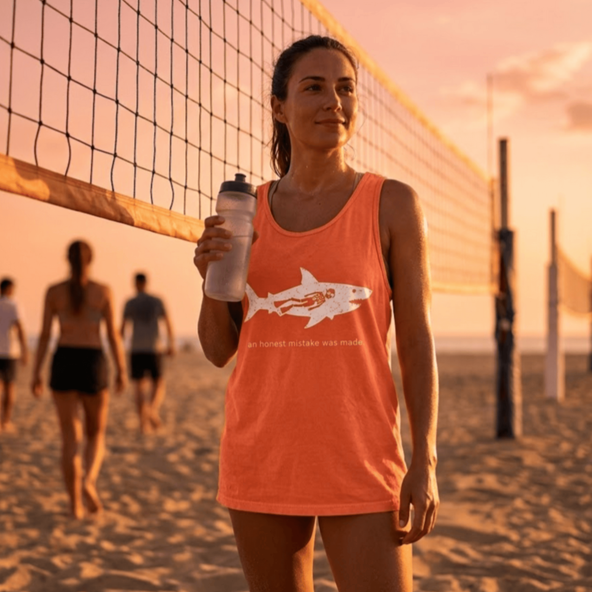 Woman wearing FullSailMarine's 'An Honest Mistake Was Made' shark tank top in coral, holding a water bottle at a beach volleyball court at sunset — women's ocean apparel.
